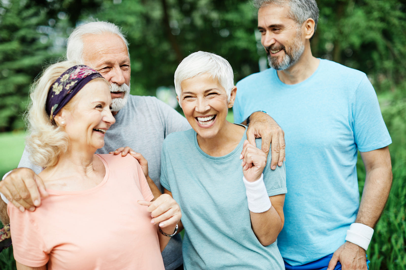 Group of four older adults smiling outdoors with greenery in the background
