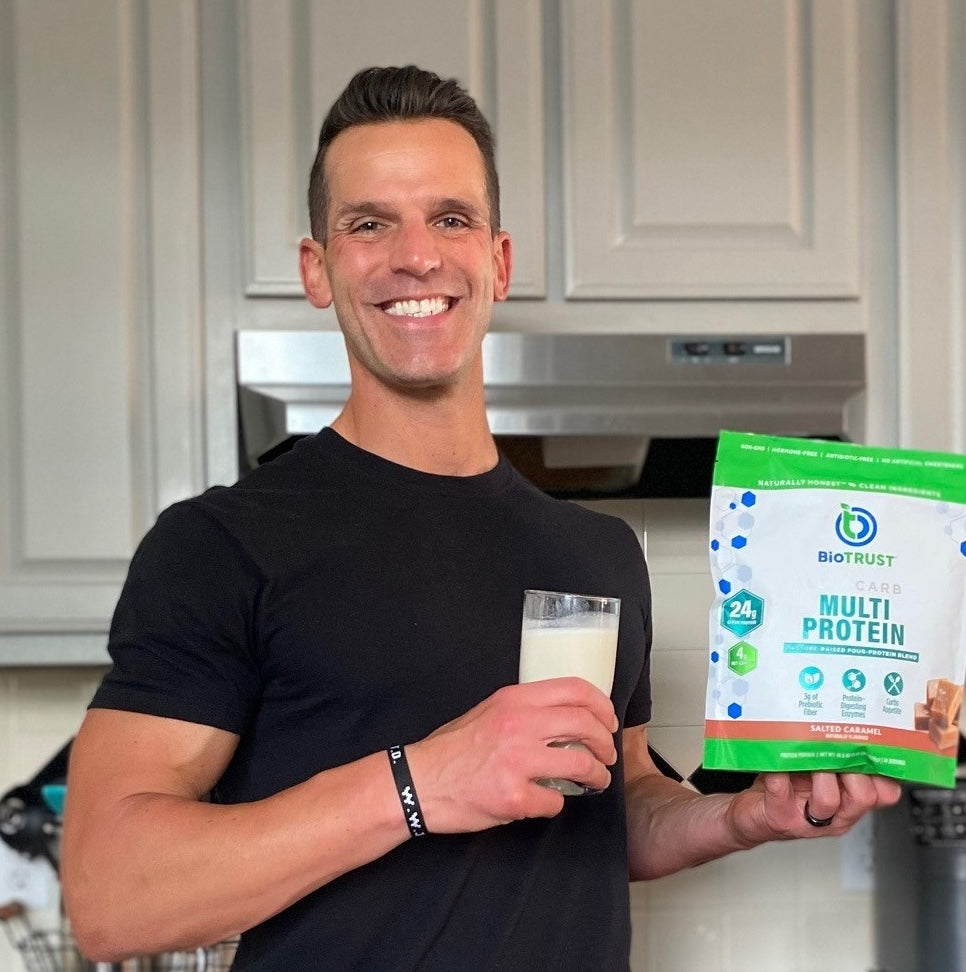 Man holding a glass of milk and a package of Biobrave Multi Protein in a kitchen.